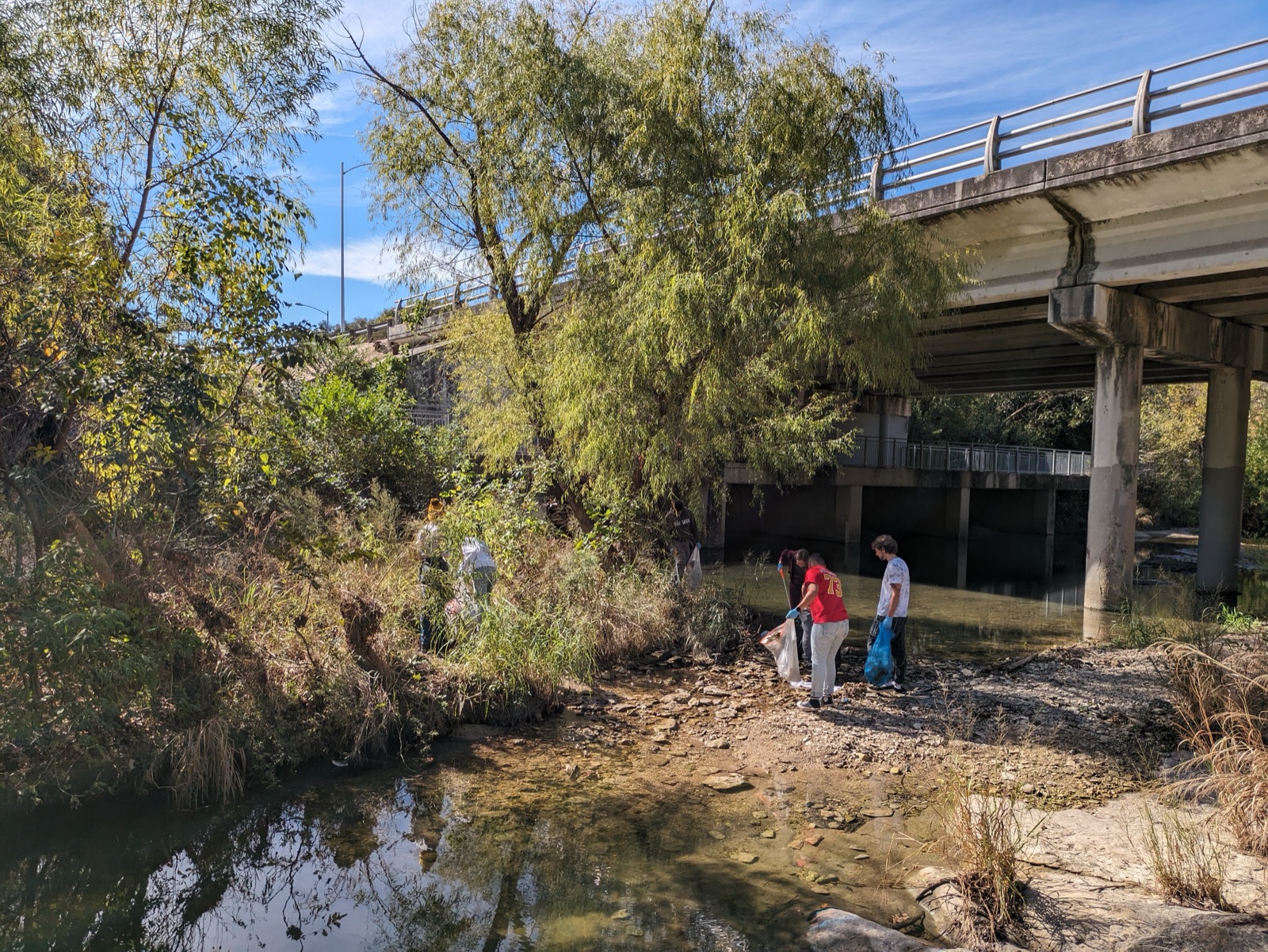 Volunteers cleaning under a bridge along an Austin creek
